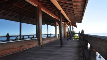 Una terraza de madera con vista al mar, sostenida por vigas y columnas, y barandilla a lo largo del borde.