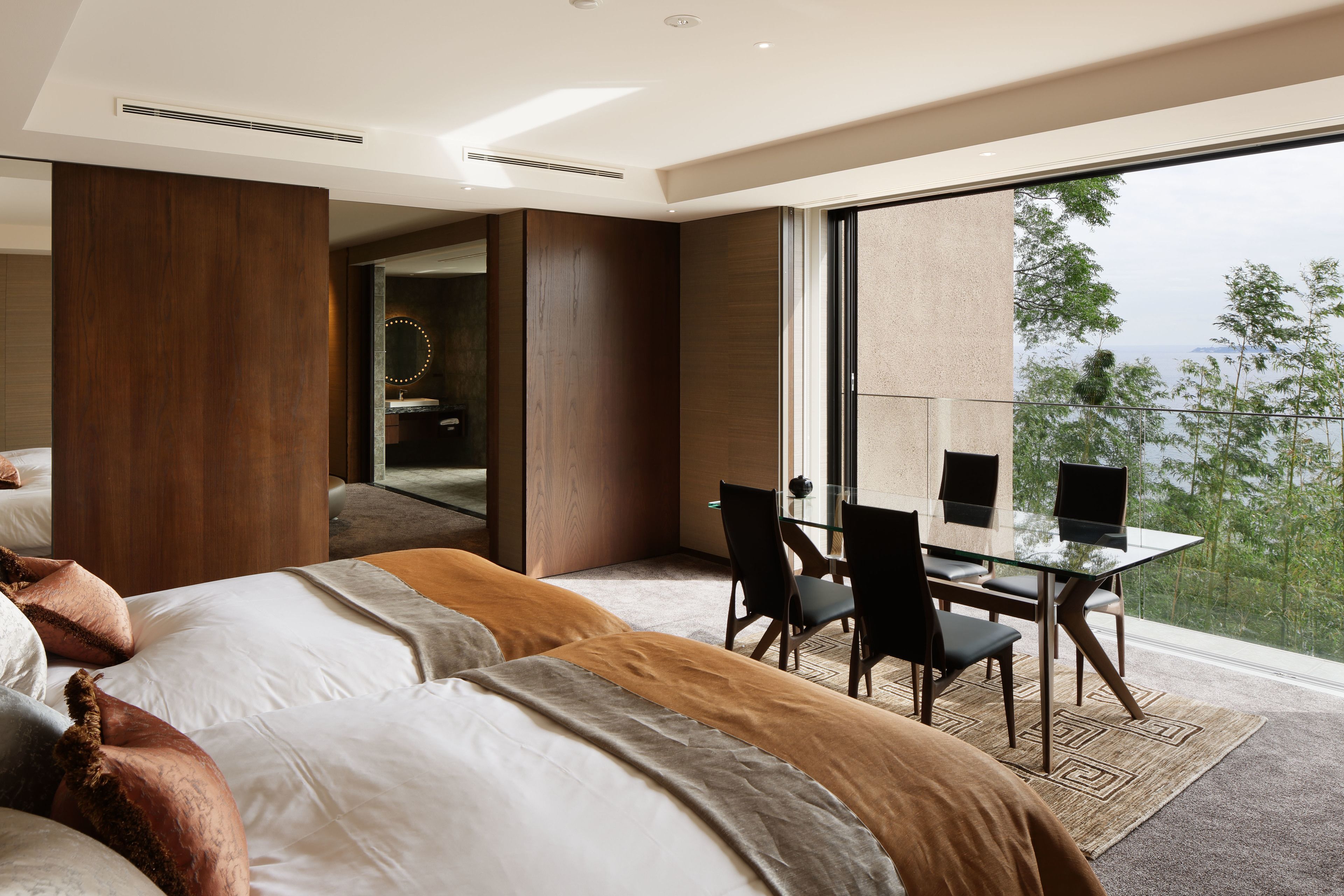 Una habitación de hotel moderna con una cama grande, una mesa de comedor de cristal con sillas y vistas al exterior.