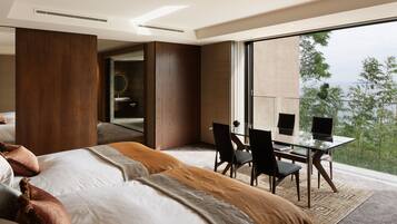 Una habitación de hotel moderna con una cama grande, una mesa de comedor de cristal con sillas y vistas al exterior.