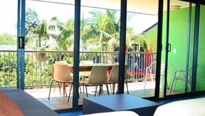 A room with a balcony, a bed, and a table with chairs. - Mooloolaba Backpackers (Mooloolaba)