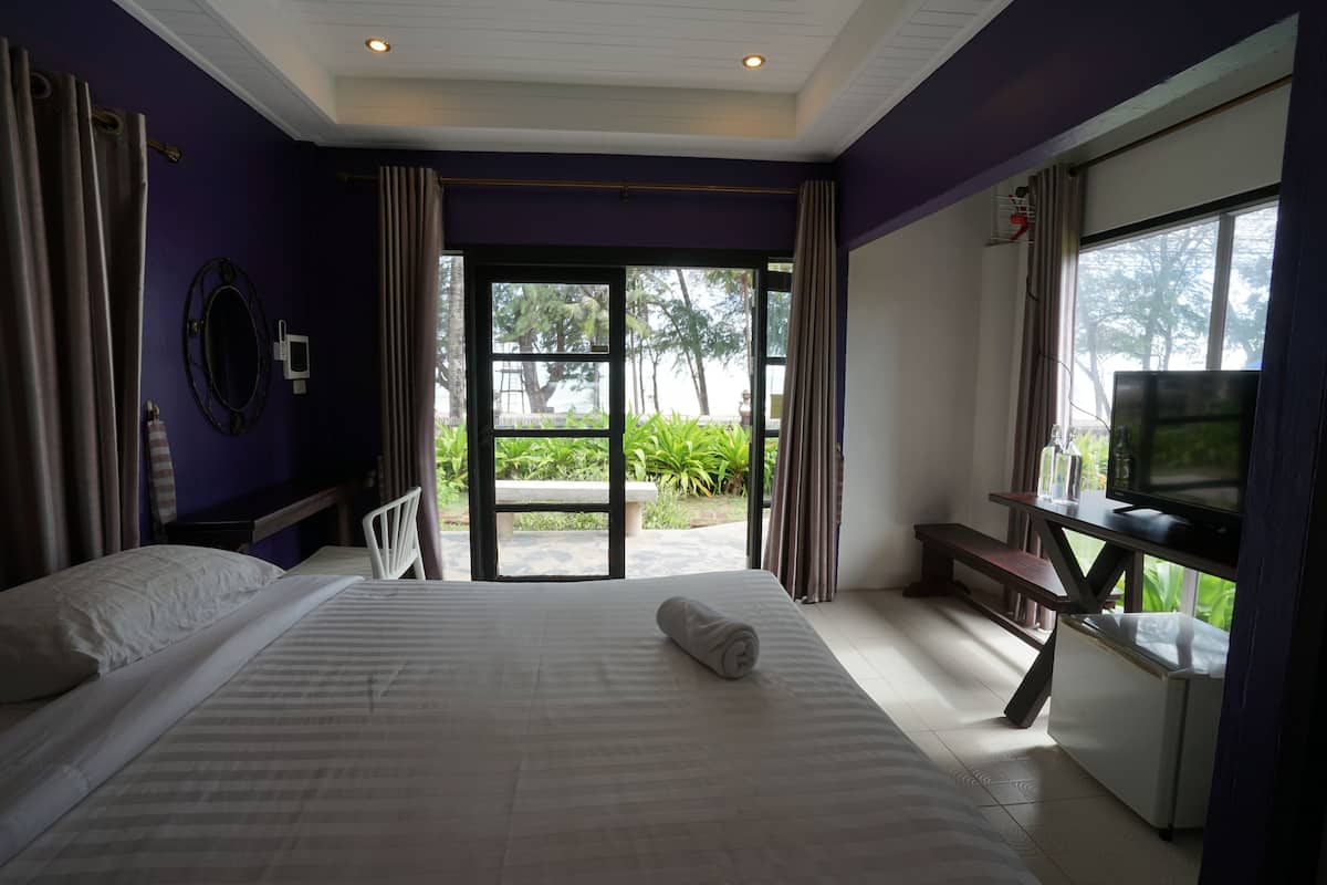 A hotel room with a bed, a desk with a television, and a view of the outdoors.
