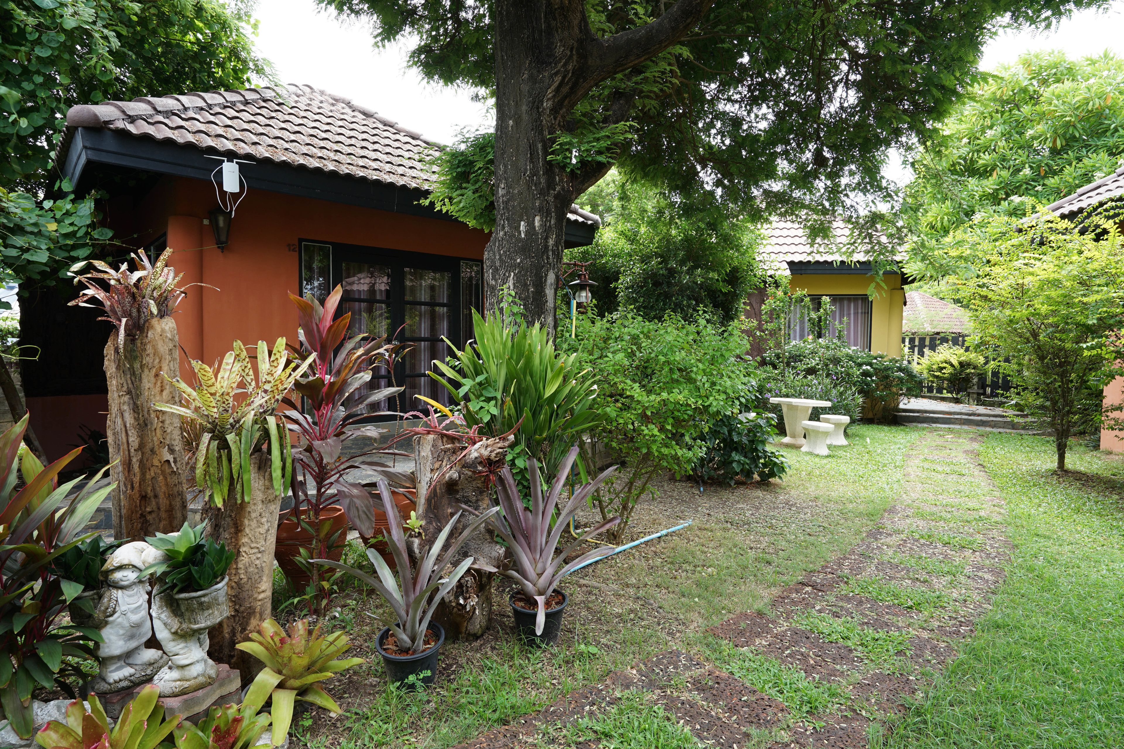 A garden with potted plants, a stone statue, and a pathway leading to a building with a tiled roof.