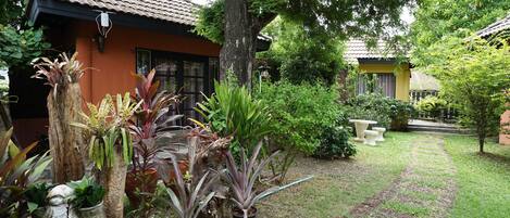 A garden with potted plants, a stone statue, and a pathway leading to a building with a tiled roof.