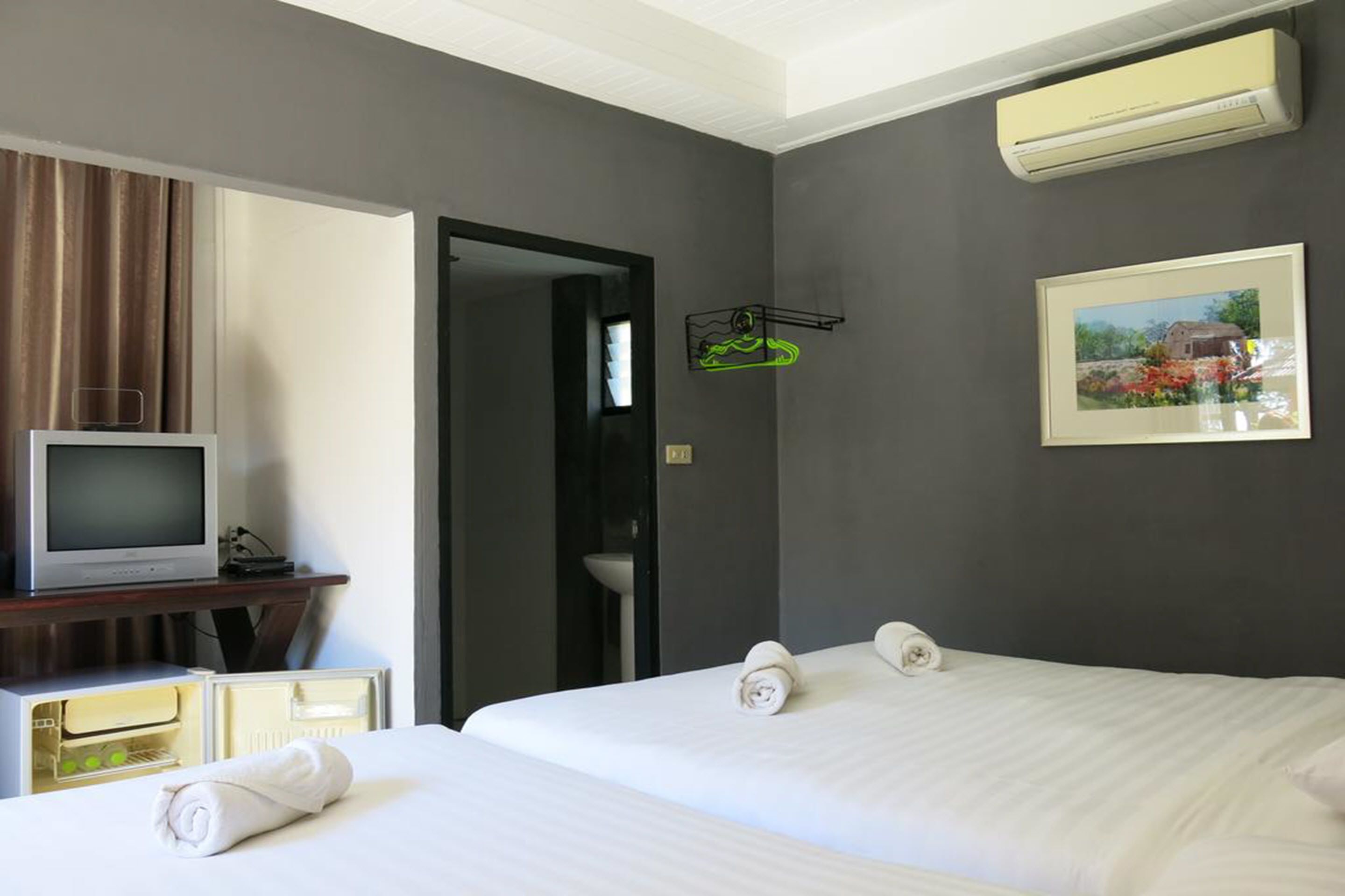 A hotel room with two beds, a television, a minibar, and an air conditioning unit.