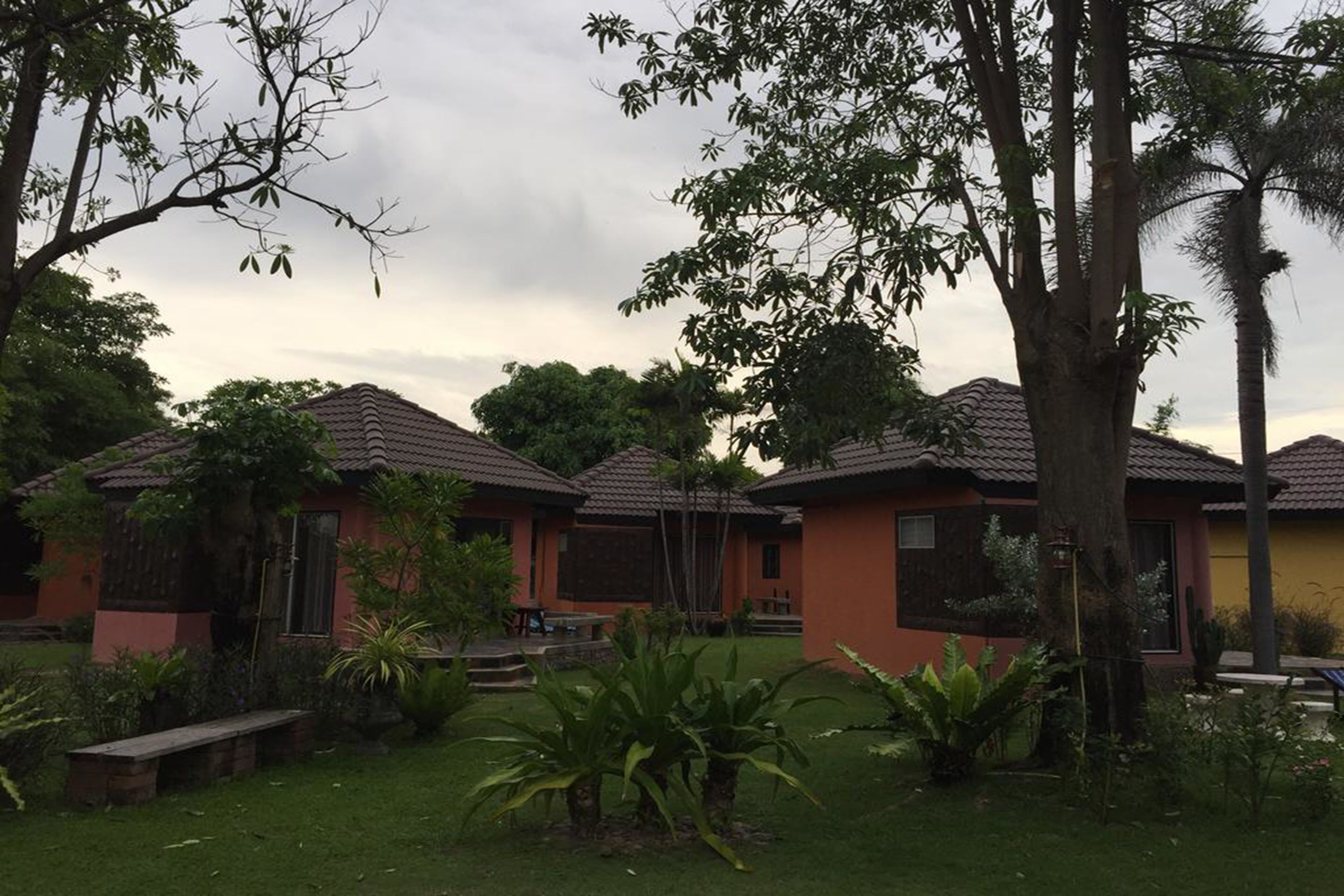 A row of single-story buildings with tiled roofs, surrounded by lush greenery and trees.