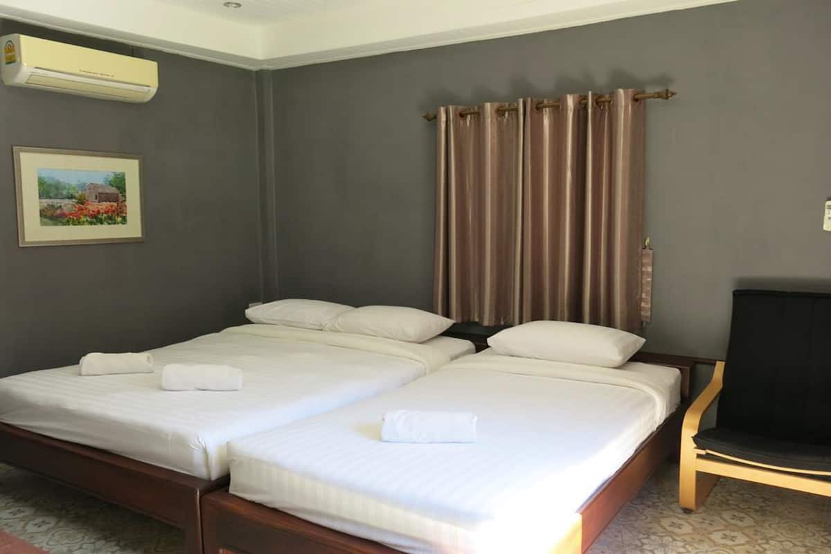 A double bed with white linens and a wooden frame, a single bed with similar features, a black chair, a wall-mounted air conditioner, and a framed picture on the wall.