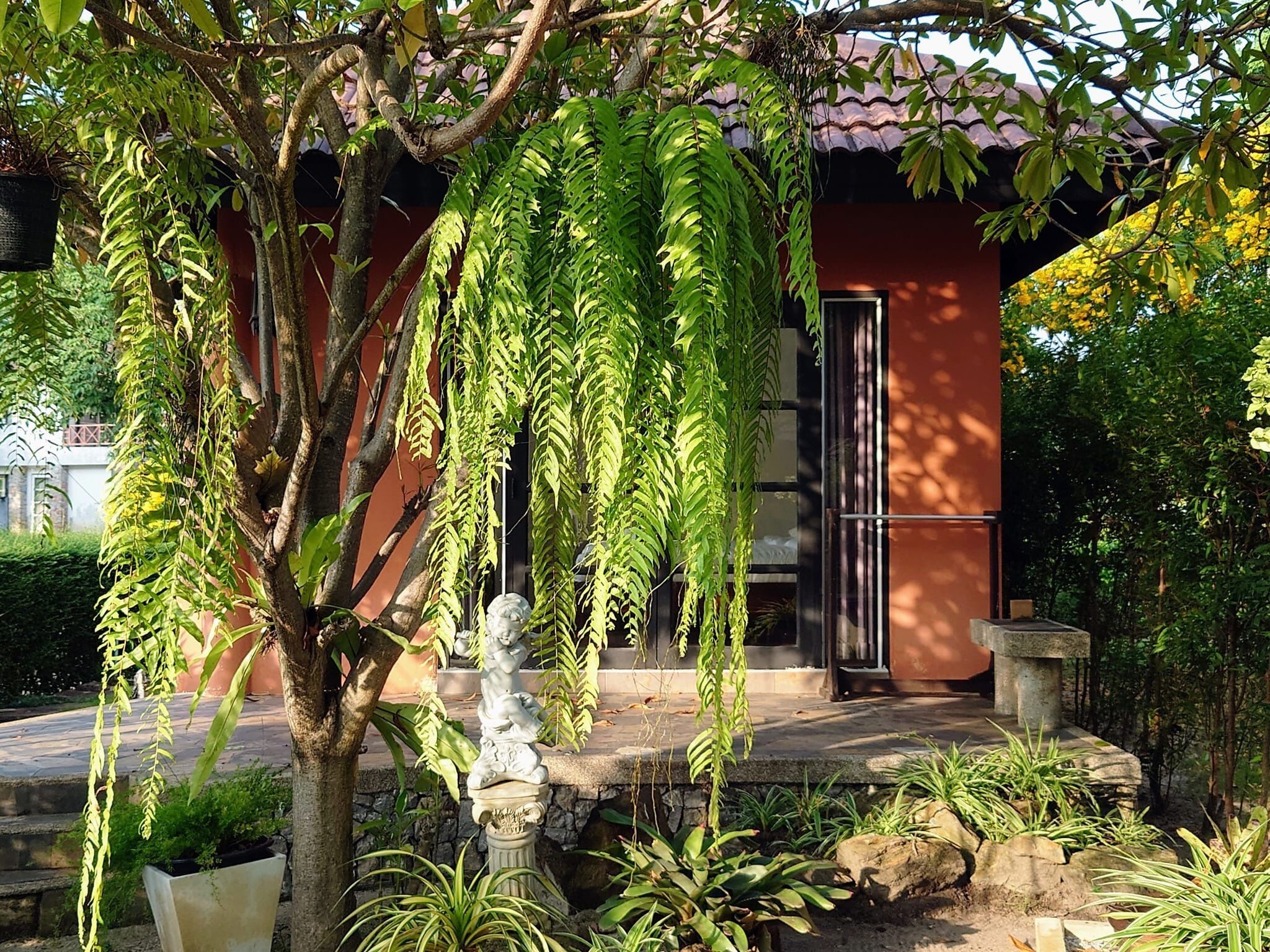 A garden with a stone statue, potted plants, and a building with a red facade.