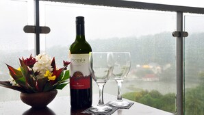 Une bouteille de vin et deux verres sur une table, avec vue sur un paysage à travers une fenêtre.
