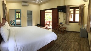 Quarto de hotel com cama, uma pequena mesa, uma cadeira, guarda-roupa e janela com cortinas.