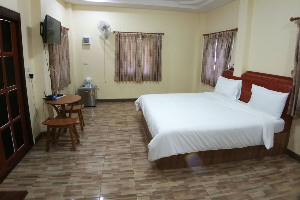 Une chambre d’hôtel équipée d’un lit, d’un bureau, d’une chaise, d’un distributeur d’eau et d’un téléviseur fixé au mur.