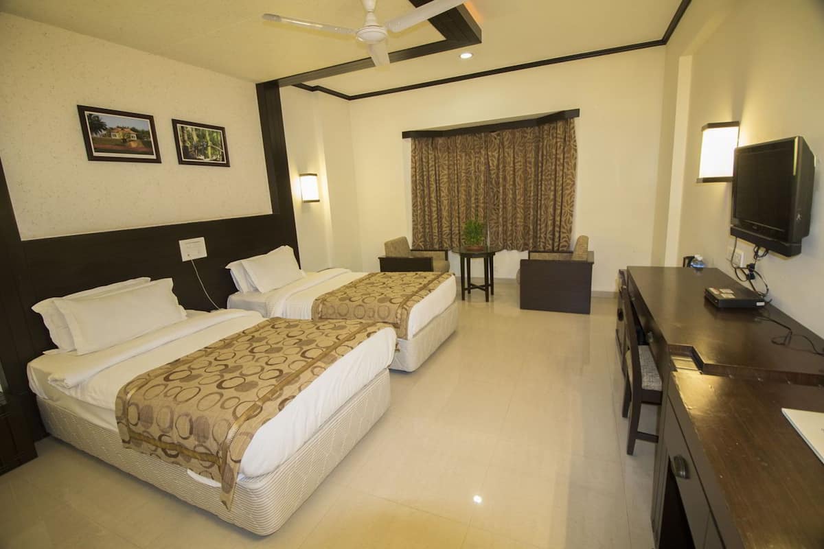 Quarto de hotel com duas camas, uma escrivaninha, uma televisão e uma janela com cortinas.
