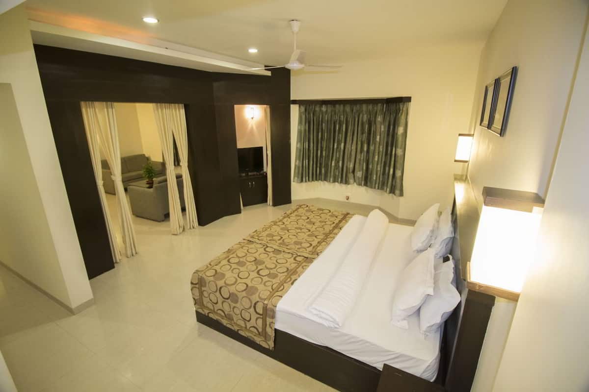 Quarto de hotel com cama, televisão, sofá e janela com cortinas.
