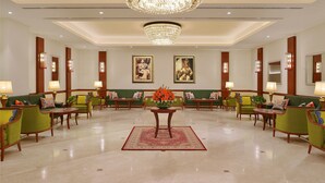 A spacious lobby with green sofas, wooden tables, and a large chandelier.