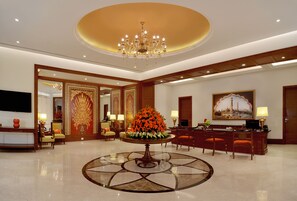A lobby with a round table, chairs, a chandelier, and a reception desk.