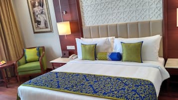 A hotel room with a large bed, a green armchair, a wall-mounted phone, and a decorative wall panel.