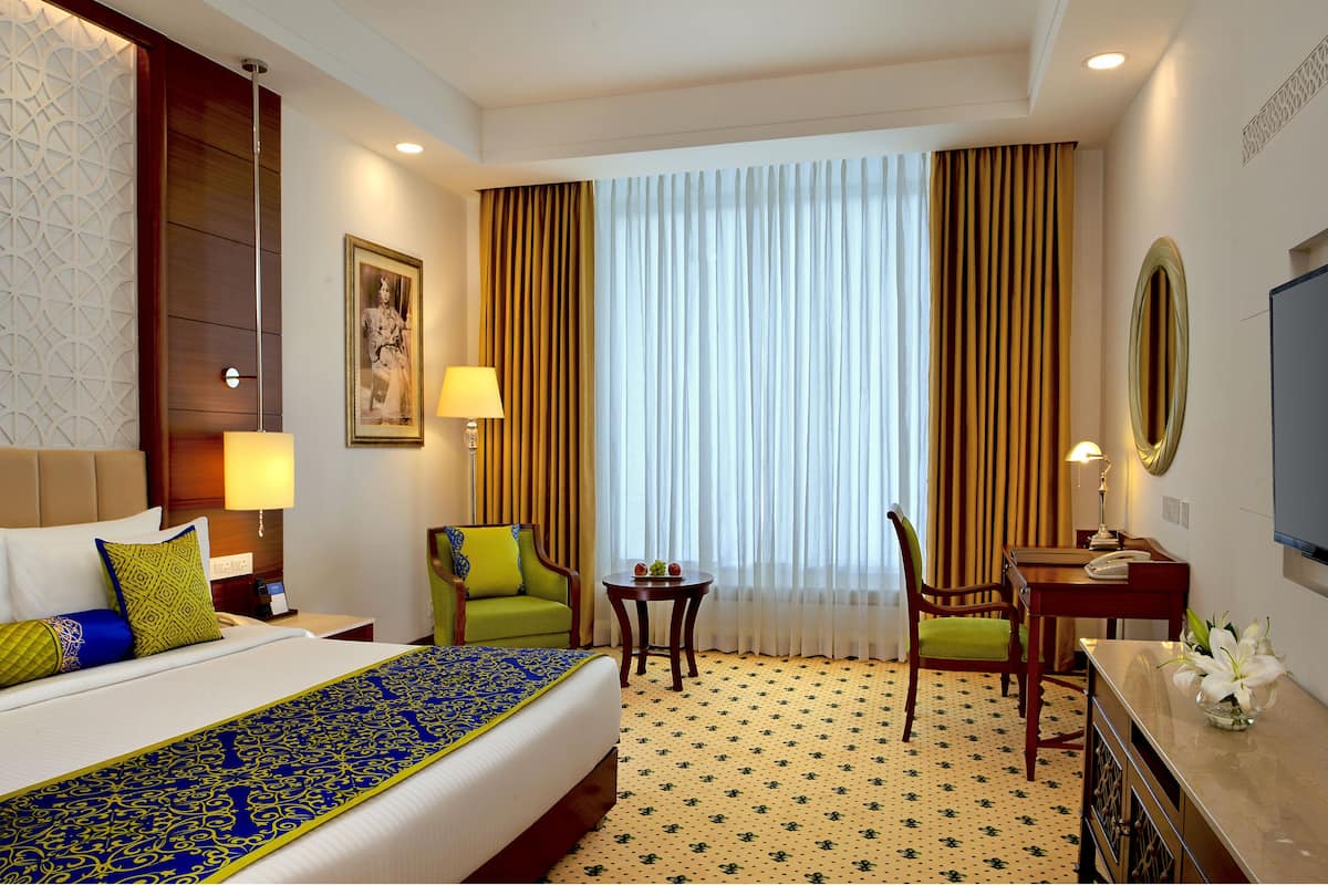 A hotel room with a bed, two chairs, a desk, a television, and a window with curtains.