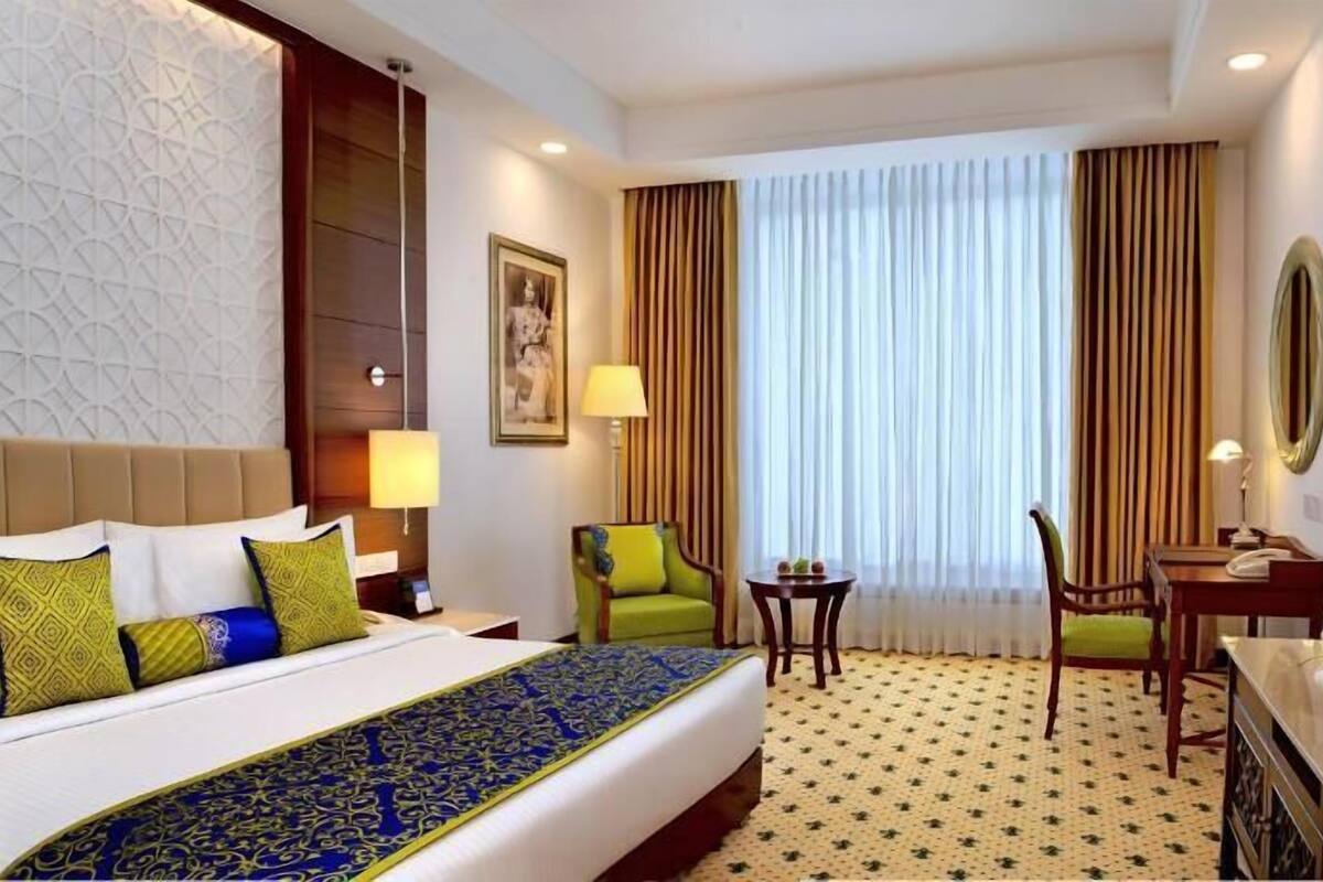 A hotel room with a bed, a desk, a chair, a TV, and a window with curtains.