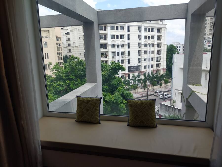 Une fenêtre agrémentée de deux coussins, donnant sur un quartier résidentiel avec des immeubles à plusieurs étages et de la verdure.