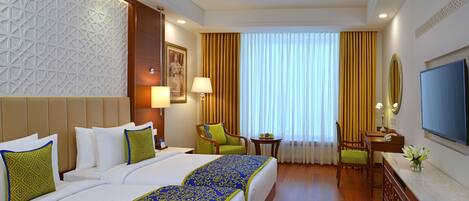 A hotel room with two beds, a desk, a chair, a TV, and a window with curtains.