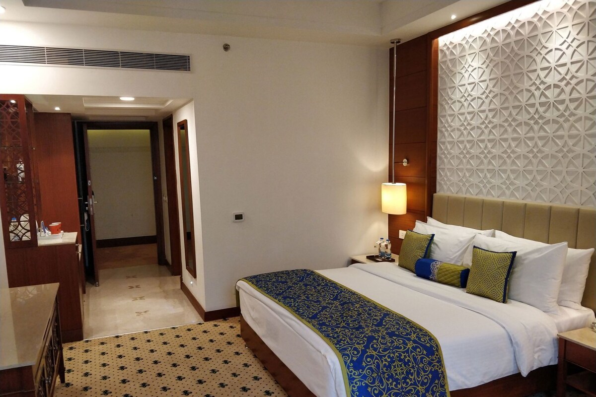 A hotel room with a bed, bedside table, lamp, and a decorative wall panel.