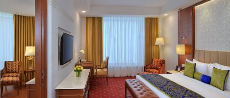 Habitación de hotel con cama, escritorio, silla, televisor y ventana con cortinas.