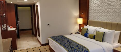 Une chambre d’hôtel avec un grand lit, une table de chevet, un mur orné d’un motif géométrique et une porte donnant sur une autre pièce.