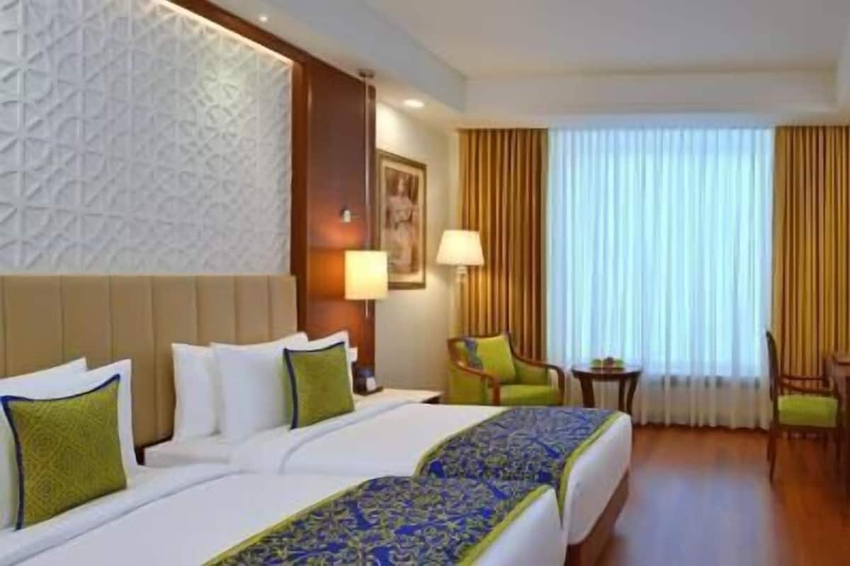 A hotel room with two beds, a desk, a chair, a TV, and a window with curtains.
