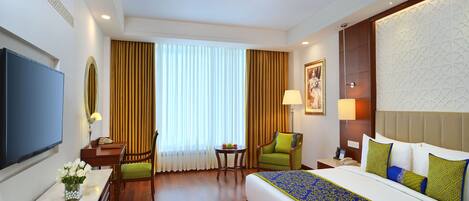 Una habitación de hotel con una cama, un escritorio con lámpara, una silla, un televisor y una ventana con cortinas.