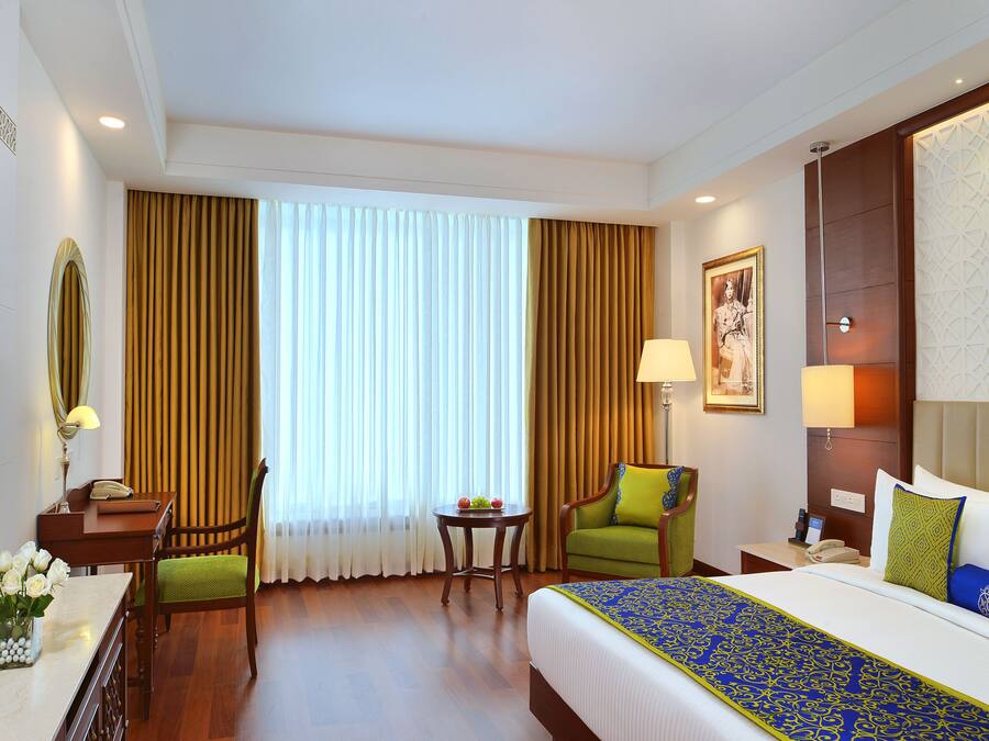 Una habitación de hotel con una cama, un escritorio con lámpara, una silla, un televisor y una ventana con cortinas.