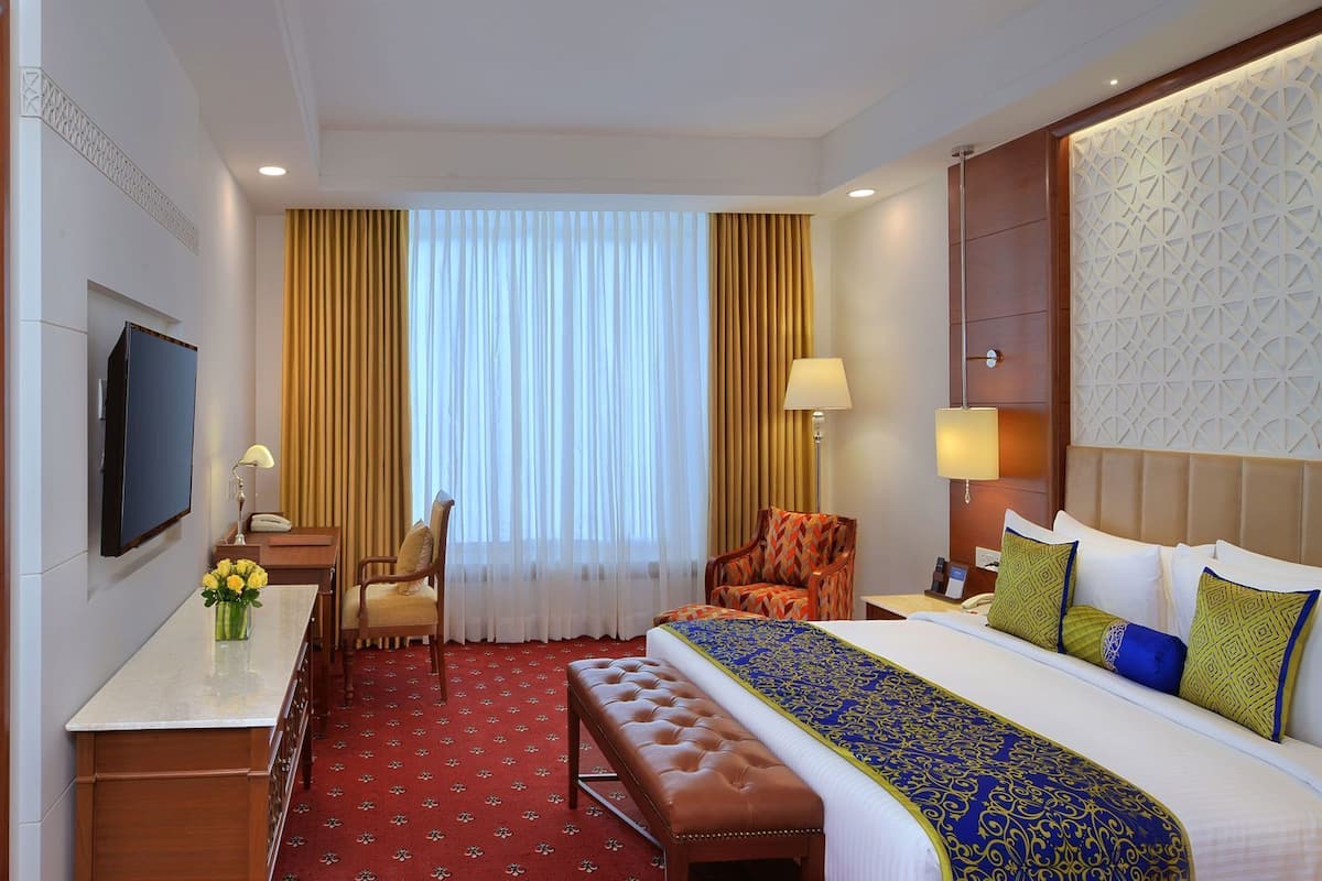A hotel room with a bed, a desk, a chair, a TV, and a window with curtains.