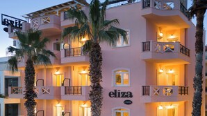 A pink multi-story hotel with balconies, outdoor seating, and palm trees. - Eliza Hotel by Panel Hospitality (Dio-Olympos)