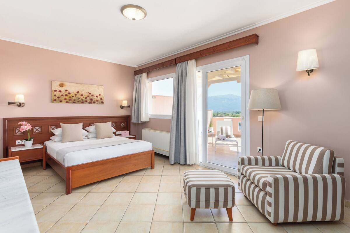 A hotel room with a bed, a sofa, a chair, a small table, and a window with curtains.