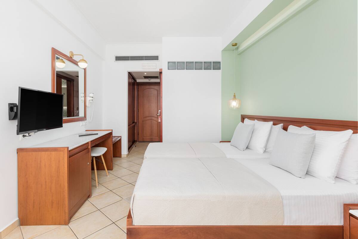 A hotel room with a bed, a desk with a chair, a television, and a mirror.
