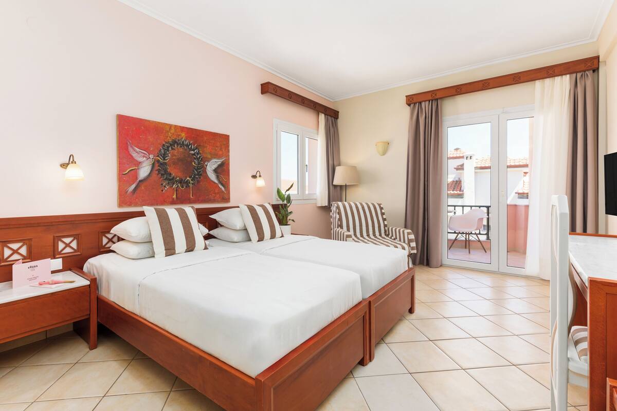 A hotel room with a double bed, a chair, a desk, a TV, and a balcony with a view.