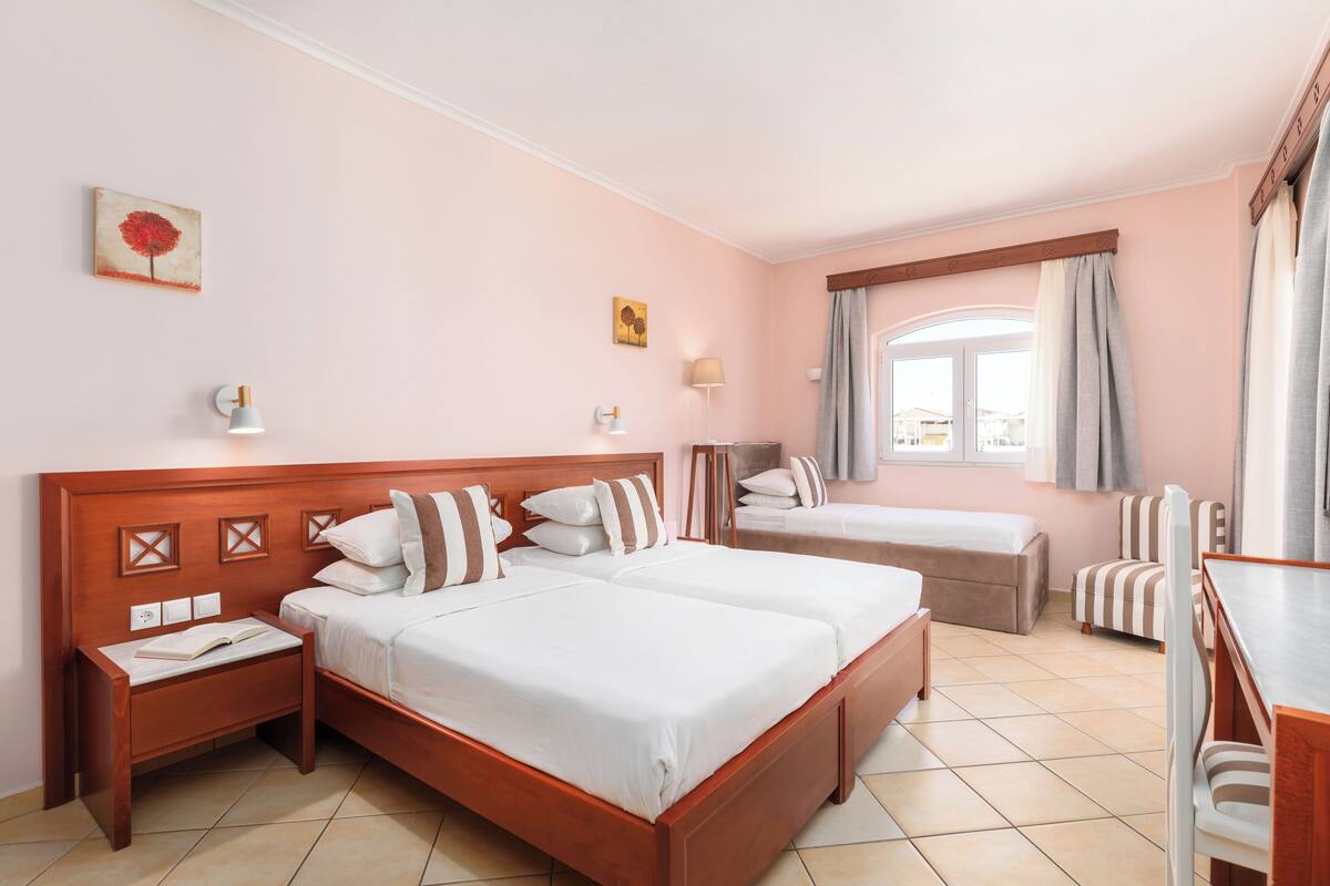 A hotel room with two beds, a desk, a chair, a nightstand, and a window with curtains.