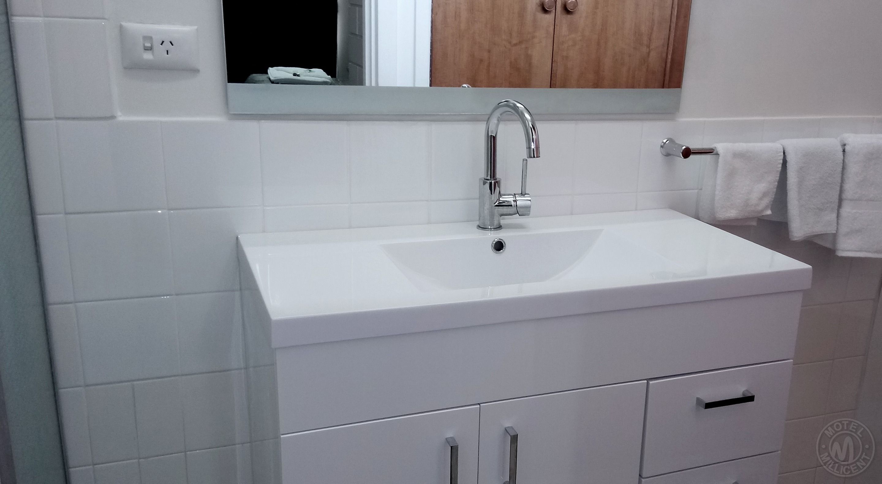 A white bathroom with a sink, mirror, and wooden cabinet above it.
