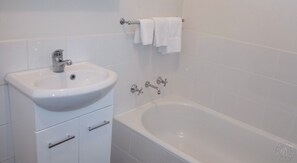 A bathroom with a white sink, a bathtub, and a towel rack. - Millicent Motel (Millicent)
