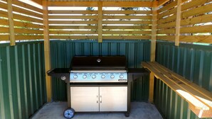 A Jumbuck portable gas grill with four burners, a stainless steel cabinet, and a black lid. - Millicent Motel (Millicent)