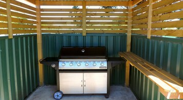 Una parrilla de gas portátil Jumbuck con cuatro quemadores, un gabinete de acero inoxidable y una tapa negra.