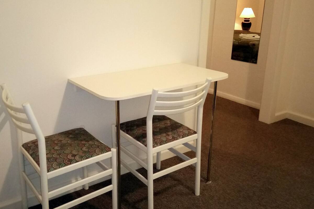 A small, white, two-seater table with a lamp on the wall behind it.
