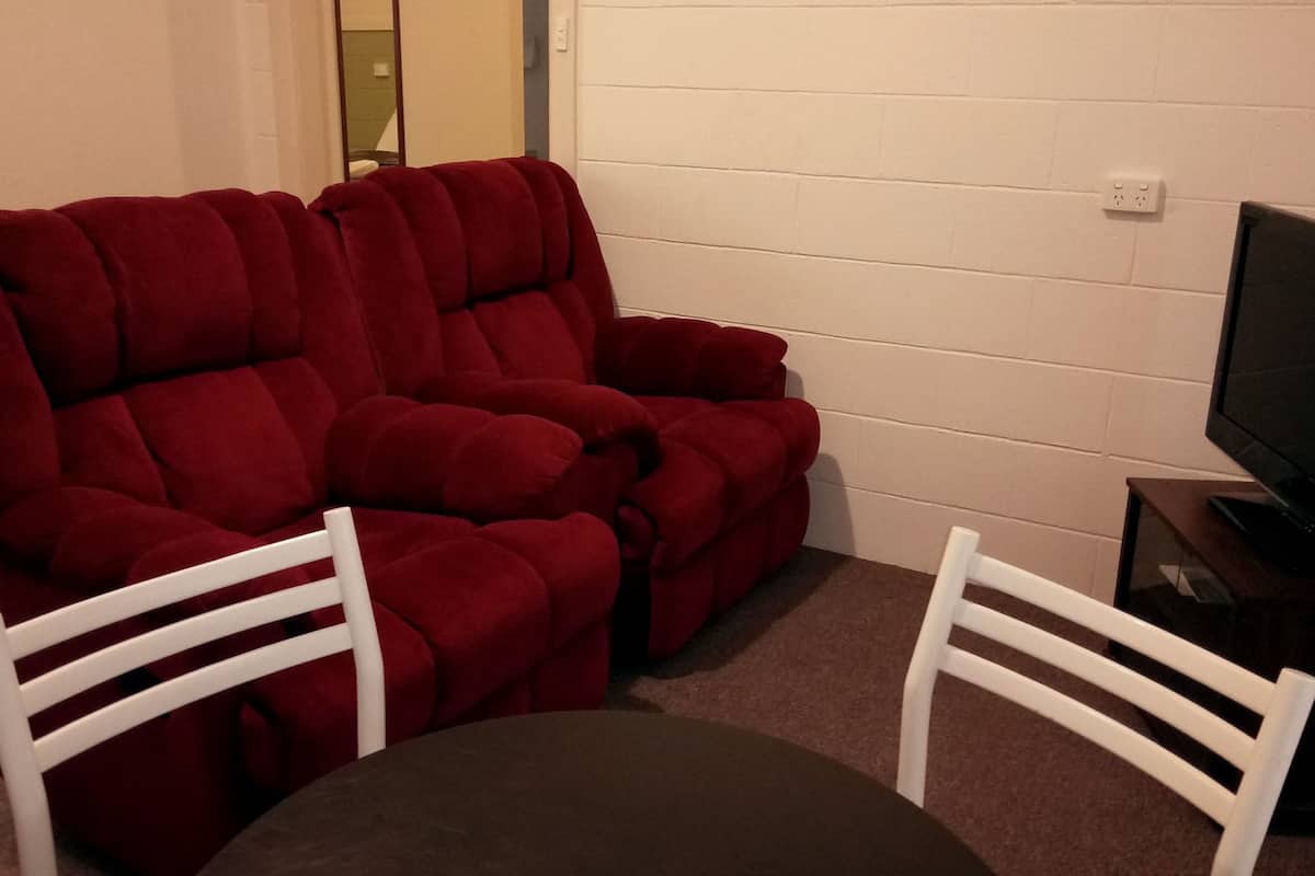A red reclining sofa with white armrests, a small table, and a television on a stand.