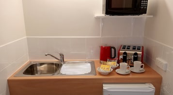 Una kitchenette con un lavamanos de acero inoxidable, una cafetera roja, un tostador y dos tazas blancas sobre una encimera de madera.
