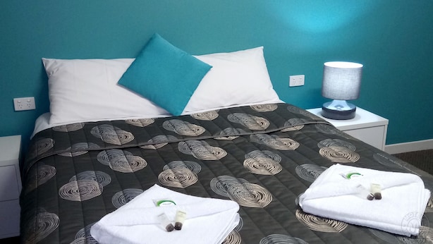 A neatly made bed with a dark patterned bedspread, two pillows, and a white towel folded on the bed. - Millicent Motel (Millicent)