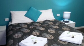 A neatly made bed with a dark patterned bedspread, two pillows, and a white towel folded on the bed. - Millicent Motel (Millicent)