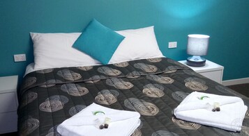 Una cama bien hecha con una colcha oscura estampada, dos almohadas y una toalla blanca doblada sobre la cama.