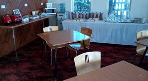 A hotel room with a wooden desk, a microwave, a water dispenser, and a breakfast bar with various food items. - Millicent Motel (Millicent)
