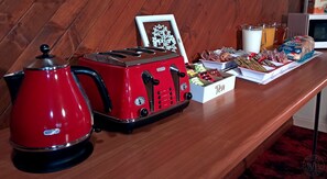 A kitchenette with a red kettle, a toaster, a framed picture, a box of tea, a glass of milk, and packaged snacks. - Millicent Motel (Millicent)