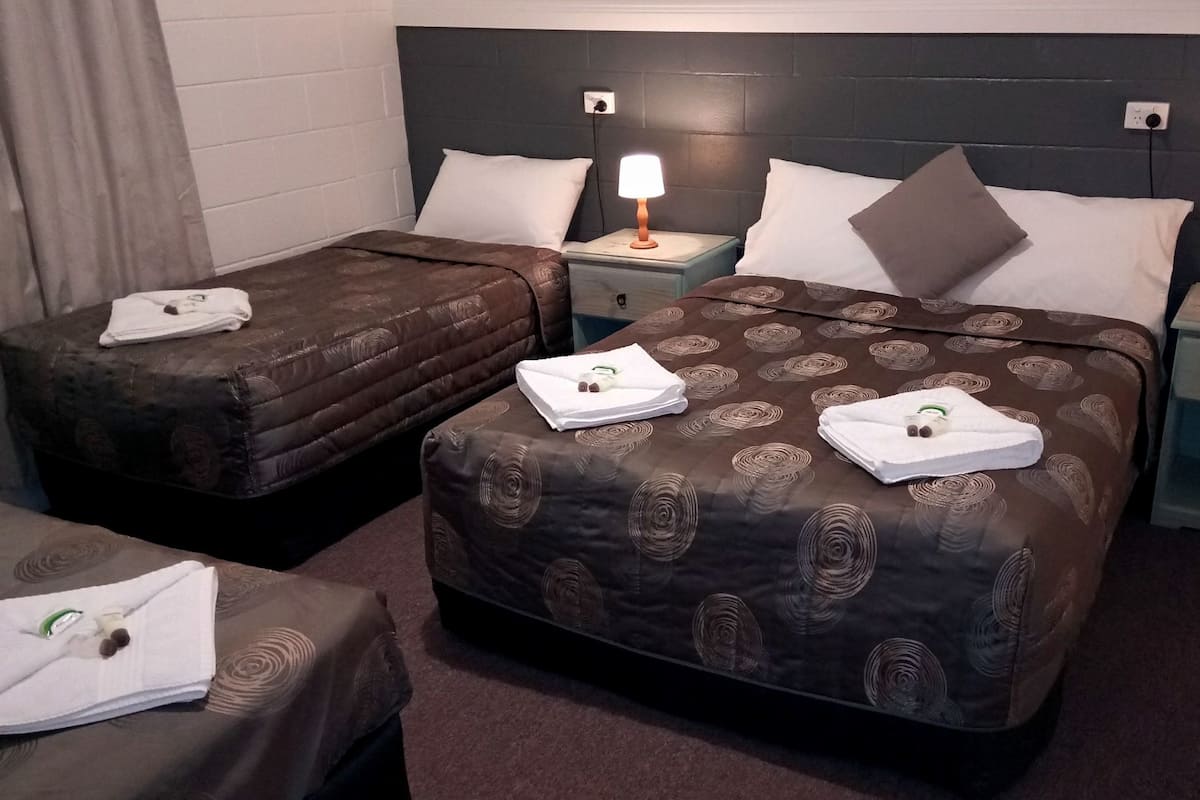 A hotel room with two beds, each with a headboard, bedside tables, and lamps.