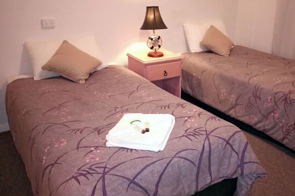 A hotel room with two beds, each with a floral-patterned bedspread and a white towel. There is a nightstand with a lamp between the beds.