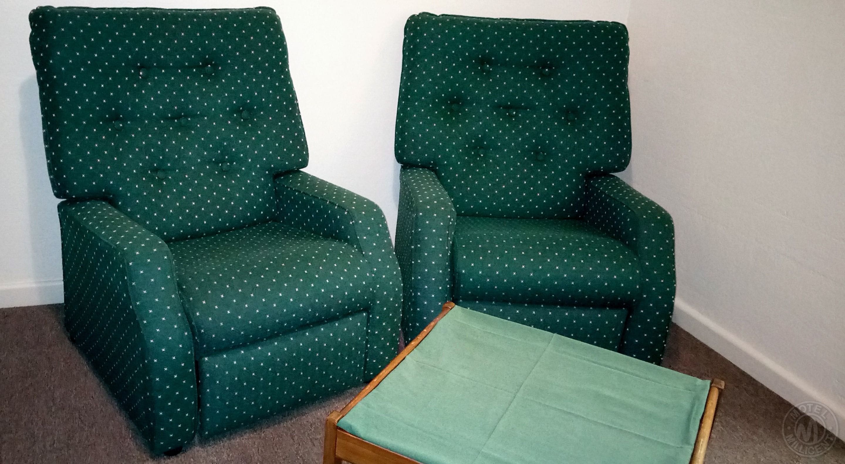 Dos sillones verdes con un estampado de estrellas, una mesita de madera y una pared blanca.